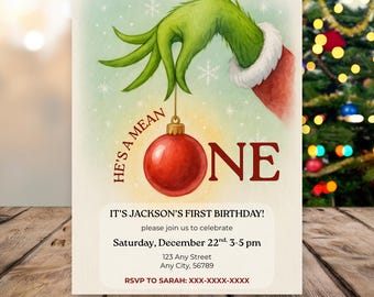 May include: A birthday invitation featuring a green hand holding a red ornament with the word "ONE". The text "HE'S A MEAN" is on the left. The invitation reads "IT'S JACKSON'S FIRST BIRTHDAY!" with event details.