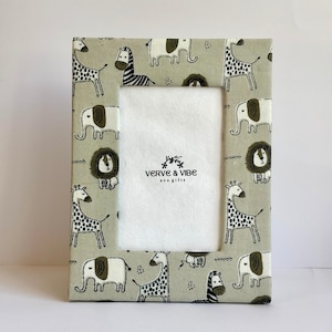 May include: Rectangular photo frame with a light green background featuring a repeating pattern of cartoon giraffes, zebras, elephants, and lions. The frame has a white interior and the text "VERVE & VIBE eco gifts".