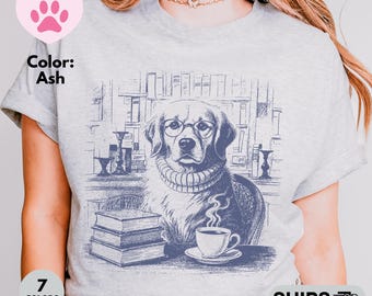 Può includere: T-shirt color cenere con un disegno blu di un cane con occhiali e un maglione, seduto a un tavolo con libri e una tazza di caffè. La maglietta ha un girocollo e maniche corte. Disponibile nelle taglie S-5XL.