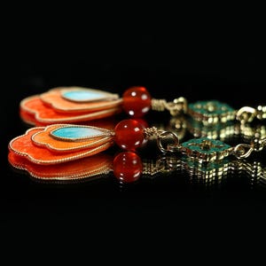 May include: A pair of gold-toned earrings with a layered, fan-shaped design in orange, with a turquoise teardrop accent. The earrings feature red beads and turquoise square accents.