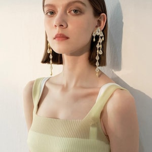 May include: Long gold-tone drop earrings featuring multiple clear, teardrop-shaped crystals suspended from a central stud. The earrings have a tiered, dangling design with alternating metallic gold teardrop accents and clear crystal stones.