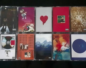 May include: A collection of ten music albums on cassette tapes. The album covers feature various designs, including a red heart, a cartoon bear, and a mountain landscape. The album titles are visible on some of the cassette tapes.