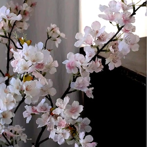 May include: Close-up of artificial cherry blossom branches with white and pink flowers. The flowers have delicate petals and are clustered along the dark brown branches. The background is a neutral gray.