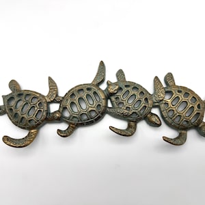 May include: A decorative metal wall art piece featuring four sea turtles linked together. The turtles have a bronze finish with a distressed, aged appearance. Each turtle has a detailed shell design and outstretched flippers.