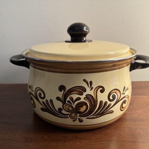 May include: A vintage enamel pot with a brown and cream floral design. The pot has a black lid with a knob.