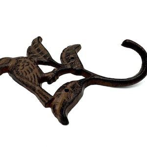 May include: A cast iron bird hook with a brown finish. The hook is shaped like a bird with its wings spread out. The hook is attached to a metal stem that curves into a hook shape.