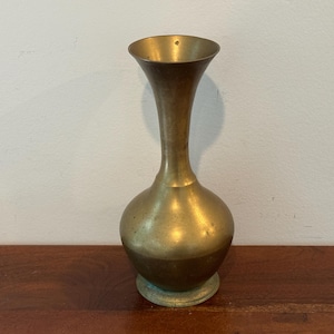 May include: A vintage brass vase with a bulbous base and a slender, flaring neck. The vase has a warm, golden hue and a slightly aged patina. It stands on a small, circular base. The vase is likely used for displaying flowers or as a decorative item.