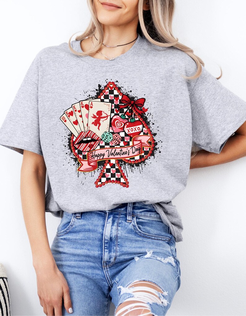 May include: A gray t-shirt featuring a Valentine's Day design. The design includes a spade shape with a red and black checkered pattern, playing cards, a cupid, hearts, and the text "Happy Valentine's Day".