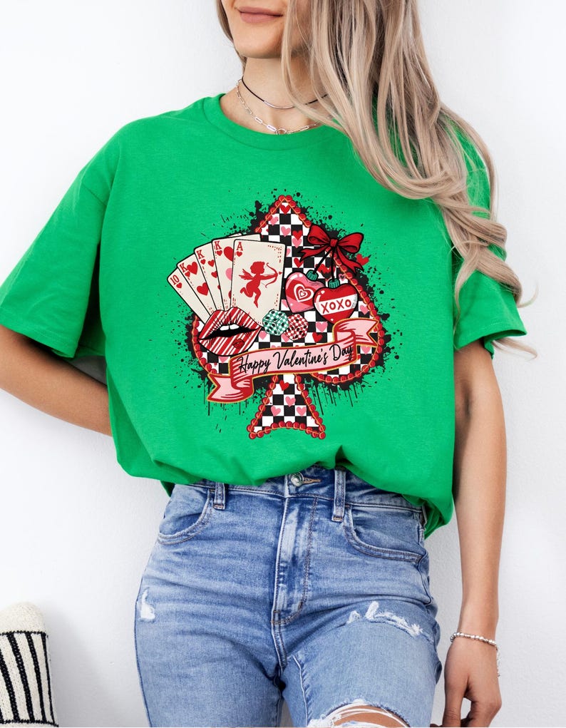 May include: A green t-shirt featuring a Valentine's Day design. The design includes a spade shape with playing cards, hearts, a cupid, and the text "Happy Valentine's Day". The design has red, black, and white accents.