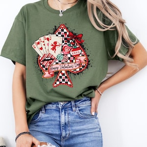 May include: Green t-shirt featuring a Valentine's Day design. The graphic includes a spade shape with playing cards, Cupid, hearts, and the text "Happy Valentine's Day." The design incorporates red, white, and black colors.