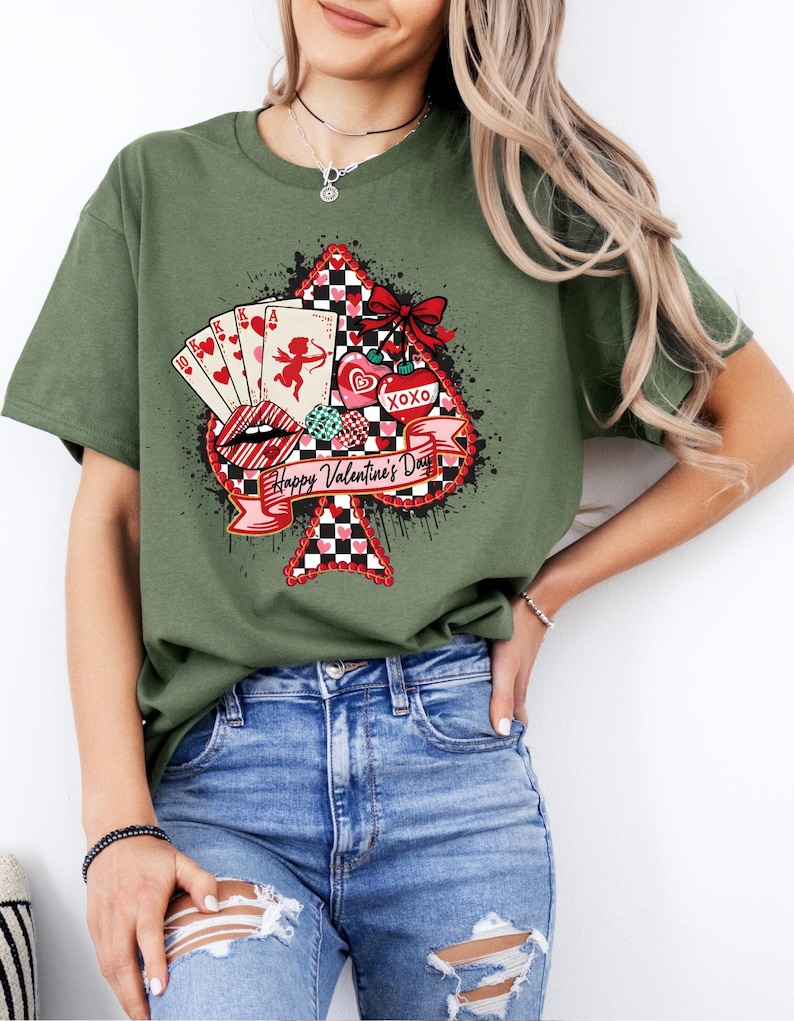 May include: Green t-shirt featuring a Valentine's Day design. The graphic includes a spade shape with playing cards, Cupid, hearts, and the text "Happy Valentine's Day." The design incorporates red, white, and black colors.