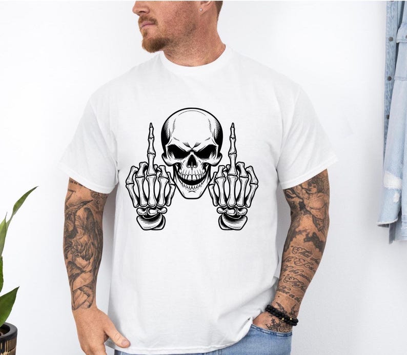 May include: White t-shirt featuring a black and white skull graphic with both hands giving the middle finger. The skull has detailed facial features and is centered on the shirt. The design is bold and graphic.