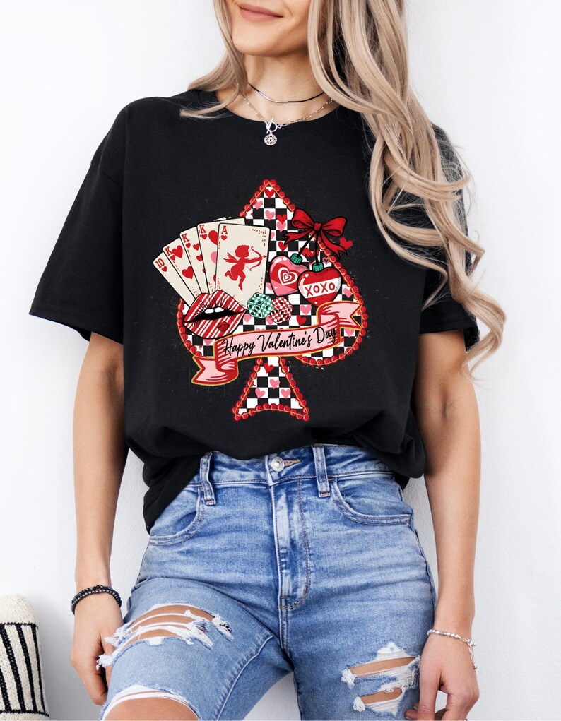 May include: Black t-shirt featuring a Valentine's Day design. The design includes a spade shape with playing cards, lips, hearts, and a bow. The words "Happy Valentine's Day" are written on a banner.