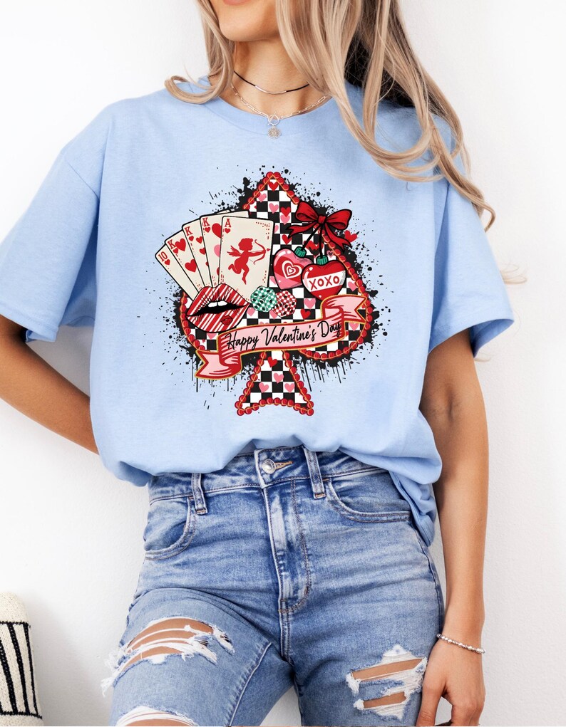 May include: A light blue t-shirt featuring a Valentine's Day design. The design includes a playing card suit shape with a red and black checkered pattern, playing cards, lips, hearts, and the text "Happy Valentine's Day".