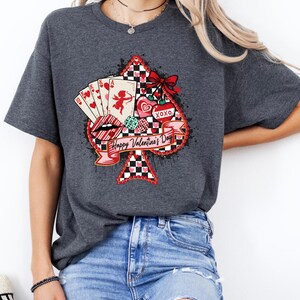 May include: Dark gray t-shirt featuring a Valentine's Day design. The graphic includes a spade shape with playing cards, lips, hearts, and the text "Happy Valentine's Day." The design incorporates red, black, and white elements.