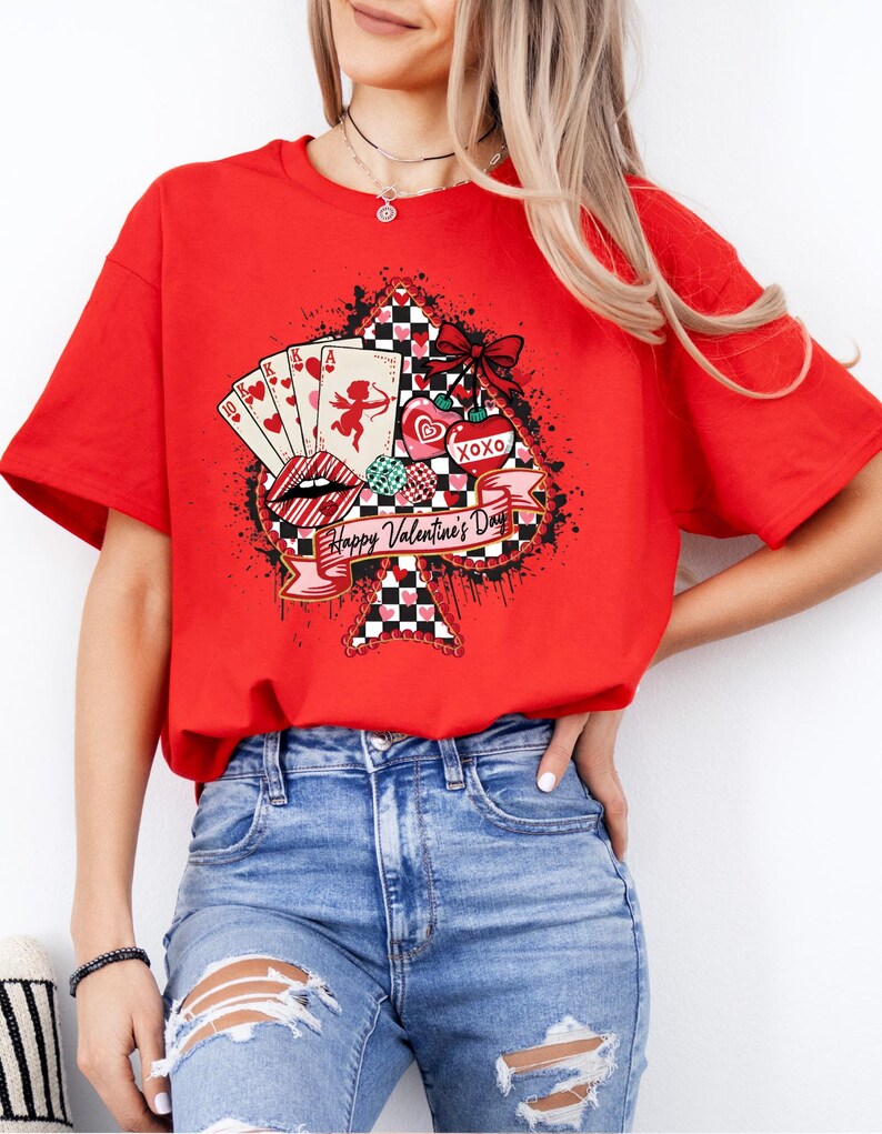 May include: A red t-shirt featuring a graphic design for Valentine's Day. The design includes playing cards, lips, hearts, and the text "Happy Valentine's Day" on a banner. The shirt has short sleeves.