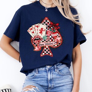 May include: Navy blue t-shirt featuring a Valentine's Day design. The graphic includes a playing card spade shape with a red bow, hearts, playing cards, and the text "Happy Valentine's Day". The shirt is a casual style.