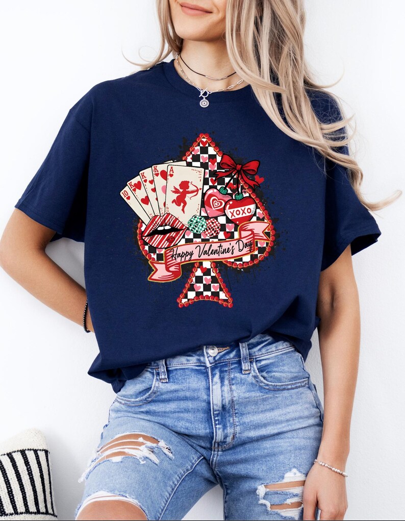 May include: Navy blue t-shirt featuring a Valentine's Day design. The graphic includes a playing card spade shape with a red bow, hearts, playing cards, and the text "Happy Valentine's Day". The shirt is a casual style.