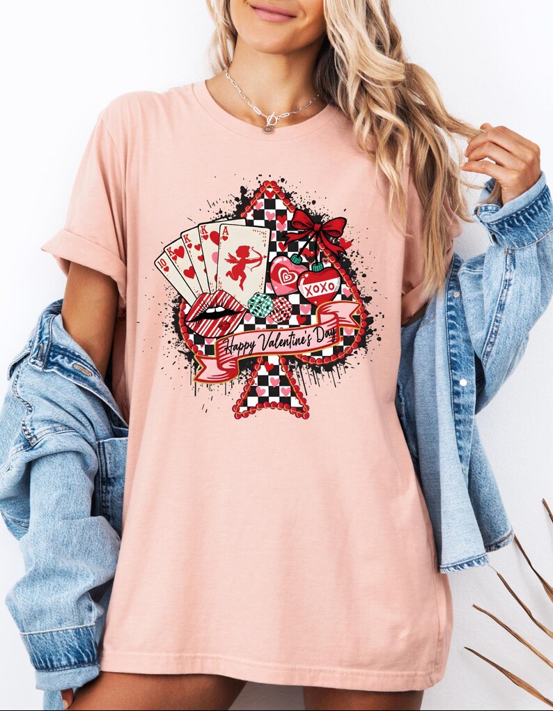 May include: A light pink t-shirt featuring a large ace of spades design with Valentine's Day graphics. The design includes playing cards, hearts, lips, and the text "Happy Valentine's Day". The shirt has rolled-up sleeves.