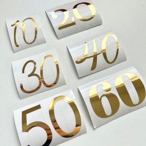 Könnte beinhalten: Sechs goldfarbene Vinyl-Aufkleber mit den Zahlen 10, 20, 30, 40, 50 und 60. Die Zahlen befinden sich auf weißem Hintergrund.
