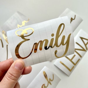 May include: Gold vinyl sticker with the name "Emily" written in a cursive font.