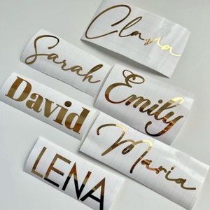 May include: Gold vinyl lettering with the names Sarah, David, Lena, Emily, Maria, and Clara. The names are on white backgrounds.
