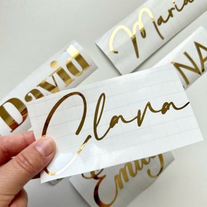 May include: Gold foil personalized name stickers with the names David,  Clara,  Maria,  Anna, and Emily.