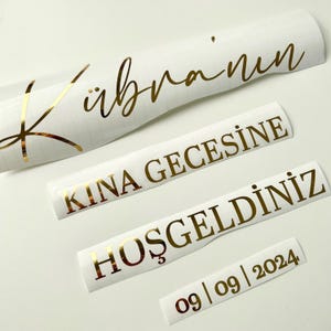 Könnte beinhalten: Goldene Folienbeschriftung auf weißem Papier lautet "Kina Gecesine Hosgeldiniz" und "09 | 09 | 2024".  Die Oberseite des Papiers lautet "[Name]" in Kursivschrift.
