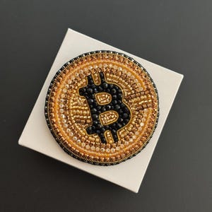 Könnte beinhalten: Eine weiße Keramik-Tasse mit schwarzem Henkel und dem Text "But First, Coffee" in fetter, schwarzer Schrift. Die Tasse steht vor einem verschwommenen Hintergrund, der eine gemütliche Umgebung suggeriert.