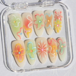 May include: A set of ten false nails with a clear base and colorful floral designs. The nails are in a clear plastic case.