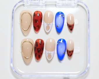 May include: A set of ten false nails in a clear plastic case. The nails are in various styles, including a gold ring, a leopard print, a white design with a pearl, and a blue ombre.