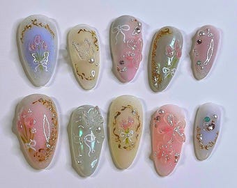 Op de afbeelding: Tien verschillende nagelontwerpen met bloemen- en vlindermotieven in pastelkleuren met gouden accenten.