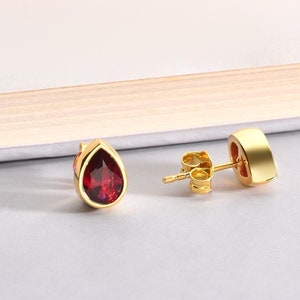 May include: A pair of gold earrings with a teardrop-shaped red gemstone.