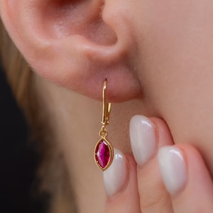 May include: A gold earring with a dangling red gemstone. The earring is a simple design with a small, oval-shaped gemstone.