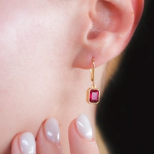 May include: Gold dangle earrings with a square red gemstone.