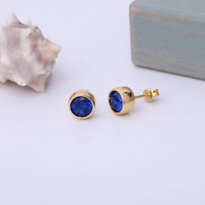Könnte beinhalten: Ein Paar goldene Ohrstecker mit blauen runden Edelsteinen.