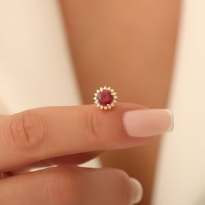 May include: A gold ring featuring a red gemstone encircled by smaller white gemstones.