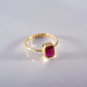 May include: A gold ring with a bright red rectangular gemstone.