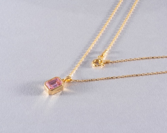 May include: A gold chain necklace with a pink gemstone pendant. The pendant is a rectangular shape with a smooth, polished surface.