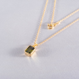 May include: A gold chain necklace with a pendant featuring a dark green rectangular gemstone.