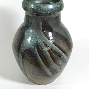 Può includere: Un vaso in ceramica con corpo arrotondato e bocca larga. Il vaso è decorato con un motivo a spirale di smalti marroni, verdi e blu.
