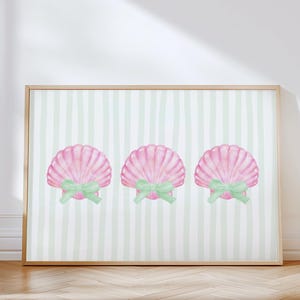 May include: A framed print featuring three pink seashell illustrations with green bows. The seashells are set against a background of vertical, light green and white stripes. The frame is a light wood color.