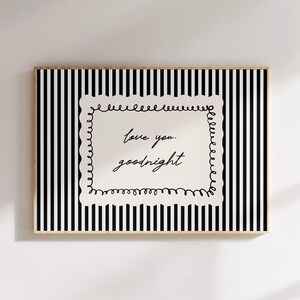 May include: Framed wall art with a black and white striped background. The artwork features a white rectangular shape with the handwritten text "love you. goodnight" in black script. The frame is a light wood color.