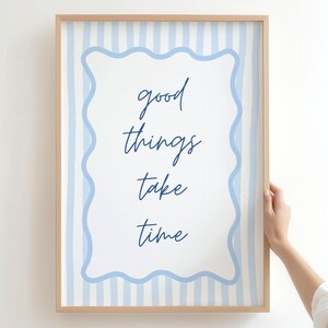 May include: A framed print with the words "good things take time" in a handwritten font. The print has a white background with blue vertical stripes and a wavy blue border. The frame is made of light-colored wood.