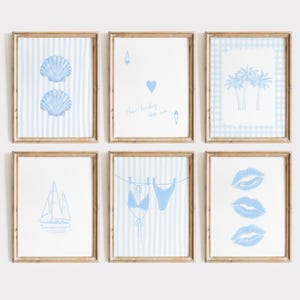Könnte beinhalten: Sechs gerahmte Kunstdrucke mit Strandmotiv. Jeder Druck zeigt eine andere blaue Illustration auf weißem Hintergrund. Die Bilder zeigen Muscheln, Spielkartensymbole, Palmen, ein Segelboot, einen Bikini und drei Lippenpaare. Die Rahmen sind hellbraun.