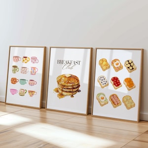 Könnte beinhalten: Drei gerahmte Aquarelldrucke. Einer zeigt verschiedene Teetassen, ein anderer Pfannkuchen mit dem Text "Breakfast Club" und der dritte Toast mit Belägen. Die Rahmen haben eine helle Holzoberfläche.