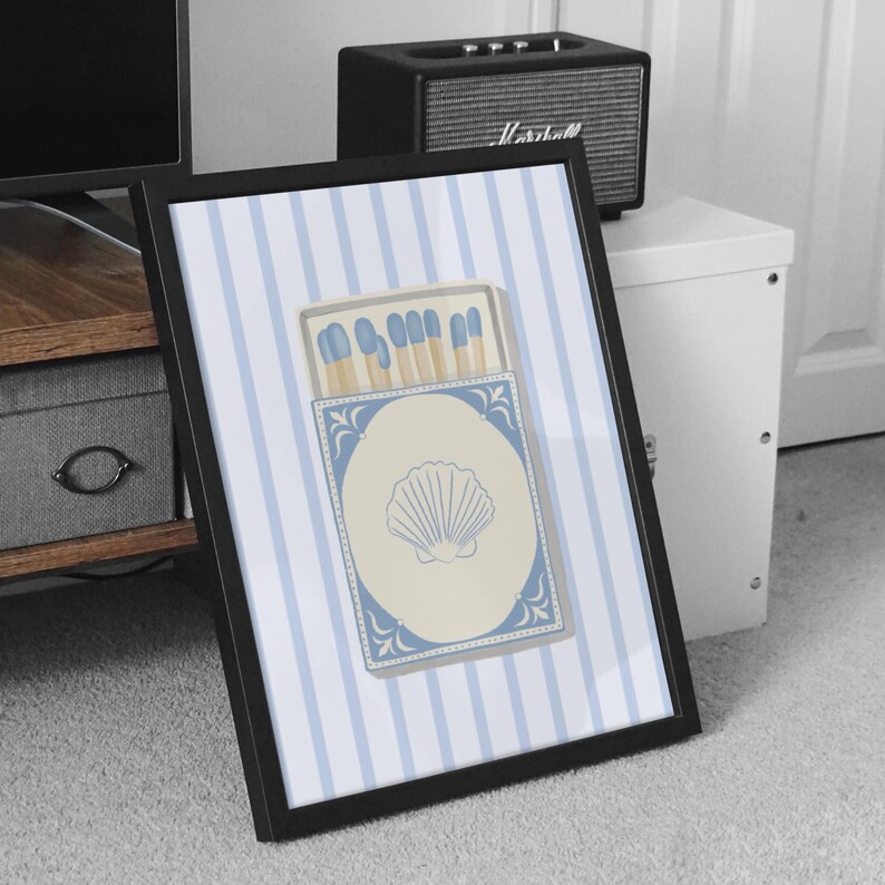 May include: A framed print of a blue and white striped background with a matchbox featuring a seashell design. The matchbox has blue and white accents and contains blue matches.