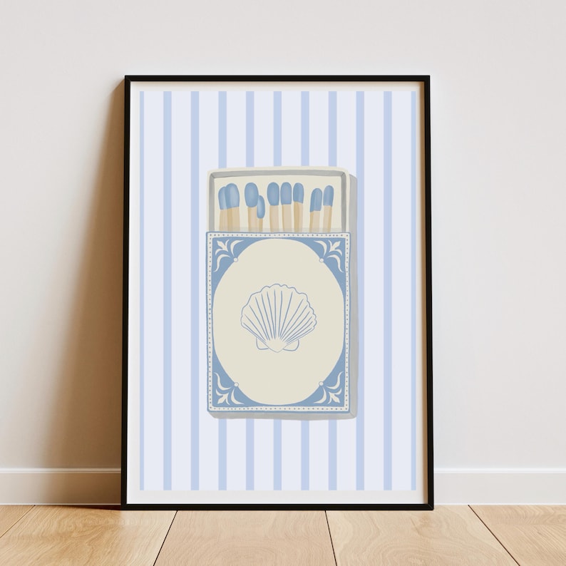 May include: A blue and white matchbox with a seashell design on the front. The matchbox is filled with matches with blue tips. The matchbox is on a background of light blue and white stripes.