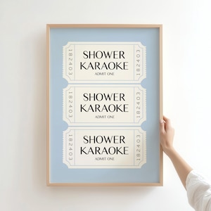 May include: A framed print featuring three vintage-style tickets with the text "SHOWER KARAOKE ADMIT ONE." The tickets are cream-colored with black text and a light blue background. The frame is a light brown color.