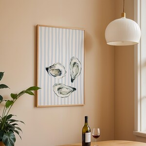 oyster print, coastal kitchen decor, watercolor seafood, preppy wall art, a watercolor painting of three oysters on the half shell, artfully arranged on a background of light blue and white vertical stripes, perfect for a beach house or kitchen.